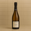 A bottle of Champagne Adrien Renoir Le Terroir Grand Cru on a beige tiled background.