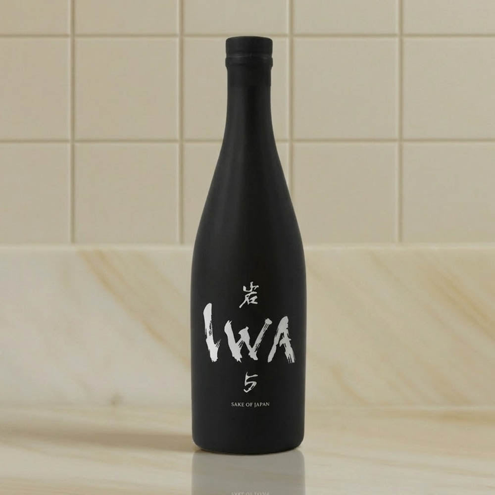 A matte black sake bottle with white Japanese calligraphy and the text '5' and 'SAKE OF JAPAN' on the front, standing on a light marble surface against a beige tiled background.