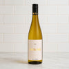 A bottle of MAC Forbes Riesling white wine stands on a light marble countertop against a white subway tile backsplash. The bottle is filled with a golden-amber liquid, has a black screw cap with gold lettering, and a cream-colored label with gold text.