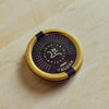 A round gold metal tin of Kaluga caviar, featuring a dark navy blue label with gold text and a small purple ribbon tied across the top, set on a light beige marble surface.