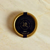 A round gold tin of Caluga Reserve 25th Anniversary smoked salmon, featuring a dark navy blue label with gold lettering, placed on a light beige marble surface.