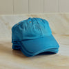 A stack of bright turquoise blue baseball caps with a small embroidered starburst on the front, displayed on a light wood surface against a tiled background.