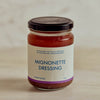 A glass jar of Portside Mignonette Dressing with a black lid and cream label, set on a light wooden surface against a neutral beige background.