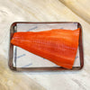 A raw salmon fillet with vibrant orange-pink flesh lies on parchment paper inside a rectangular metal baking tray, set on a light beige marble surface.
