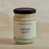 A glass jar of Portside Tartare Sauce with a cream-colored label and a dark purple lid, set against a neutral, light beige background.