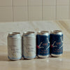 Four craft beer cans from UNI and Sea Bird lined up on a light marble countertop against a tiled backsplash. The cans feature artistic blue, white, and gold designs with seagulls.