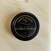 A round black tin of Yarra Valley First Harvest Salmon Pearls, featuring gold lettering and a gold fish logo, set against a light beige marble background.